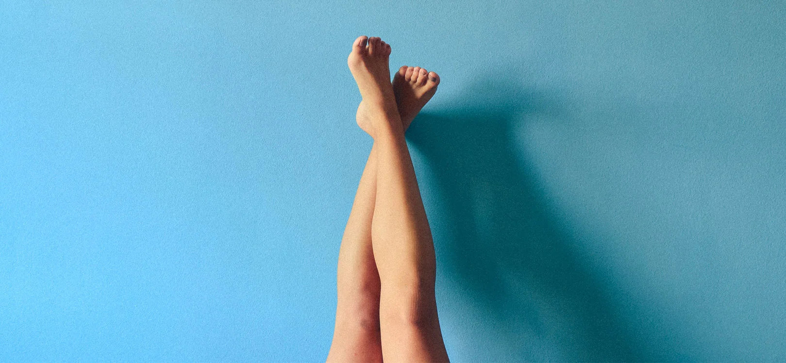 Two legs crossed and raised up against a blue wall