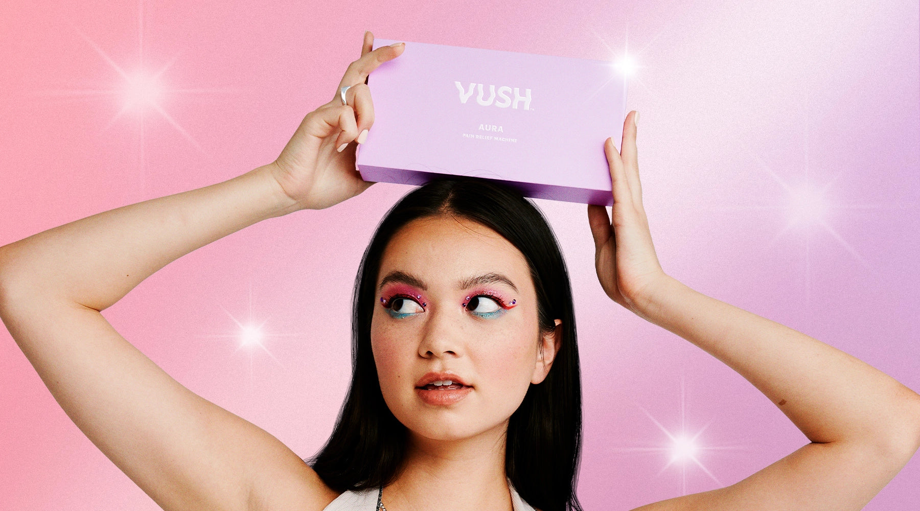 Young woman with long dark hair posing with VUSH purple Aura box above head against pink/purple background with sparkly white stars